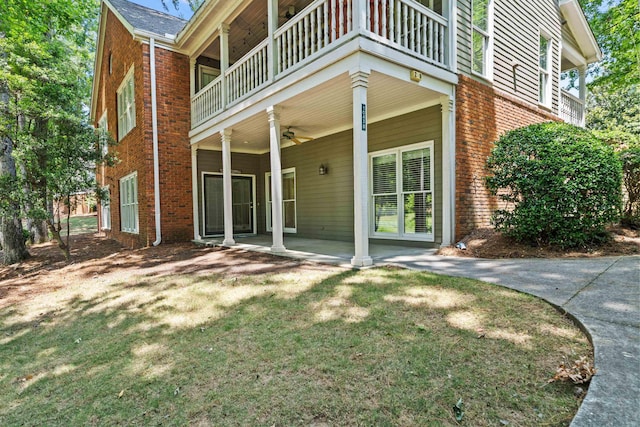 rear view of property with ceiling fan, a lawn, and a balcony