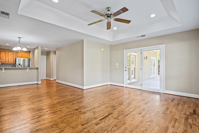 unfurnished living room with a raised ceiling, wood-type flooring, and ceiling fan with notable chandelier