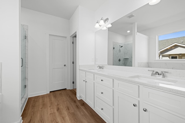 bathroom with double vanity, wood finished floors, a sink, and a marble finish shower