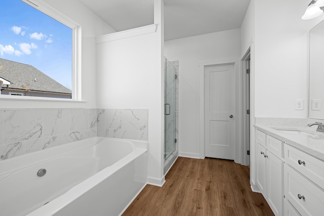 bathroom featuring wood finished floors, a stall shower, a garden tub, and vanity