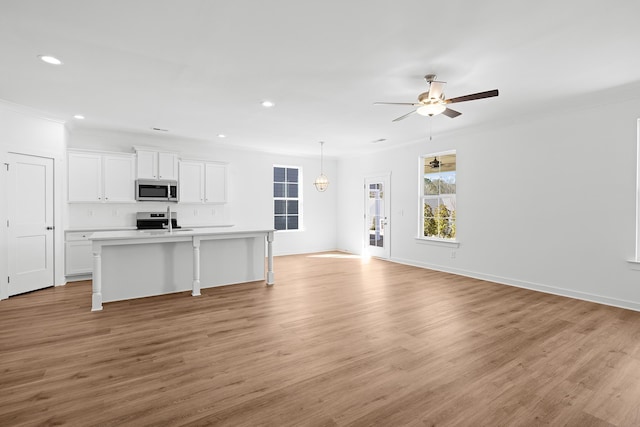 kitchen with white cabinets, an island with sink, open floor plan, stainless steel appliances, and light wood-type flooring