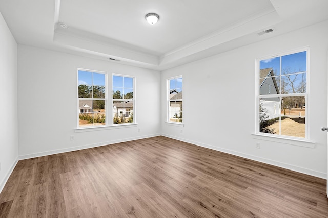 empty room with wood finished floors, a raised ceiling, visible vents, and baseboards