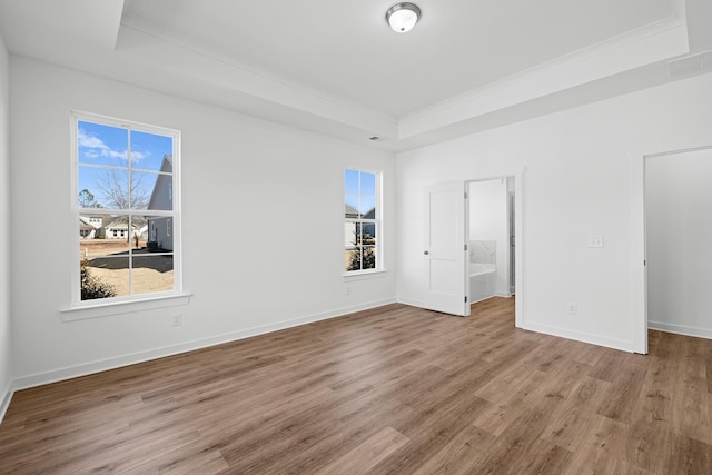 unfurnished bedroom with crown molding, a raised ceiling, ensuite bath, wood finished floors, and baseboards