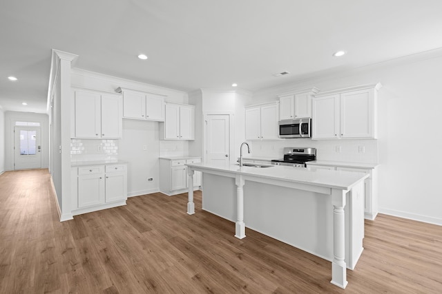 kitchen with decorative backsplash, appliances with stainless steel finishes, light wood-style floors, white cabinets, and an island with sink