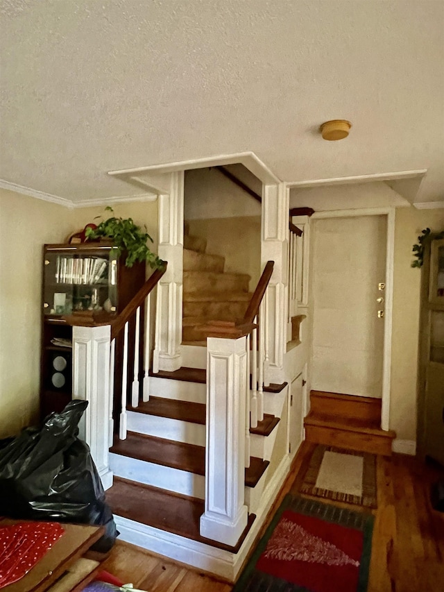 stairway with hardwood / wood-style flooring, crown molding, and a textured ceiling