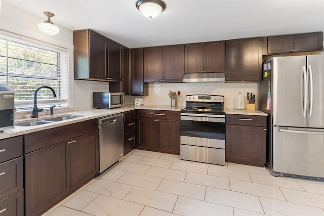 kitchen with appliances with stainless steel finishes, sink, light stone counters, and dark brown cabinets