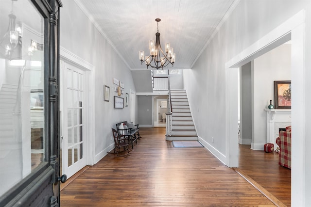 foyer entrance with a fireplace, a notable chandelier, dark wood-type flooring, and ornamental molding