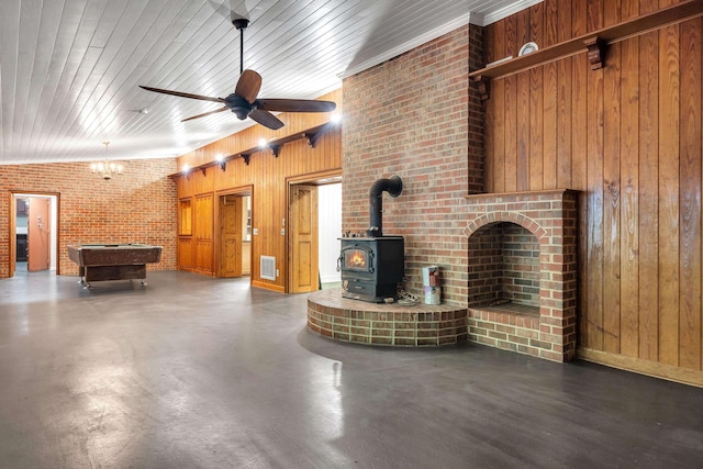 unfurnished living room with brick wall, wooden walls, billiards, a wood stove, and ceiling fan