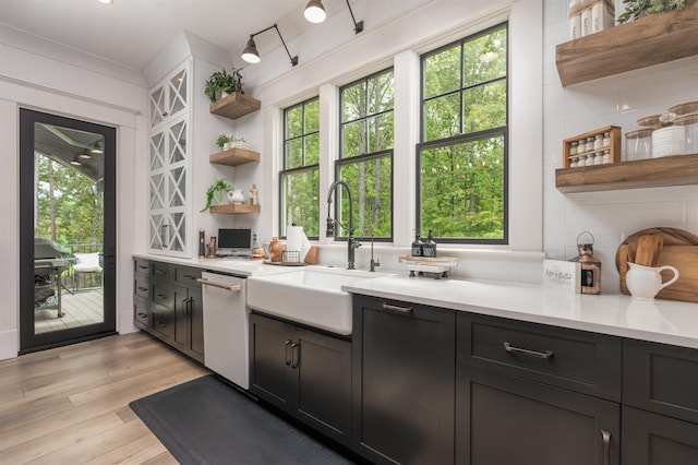 bar featuring tasteful backsplash, sink, dishwasher, and light wood-type flooring