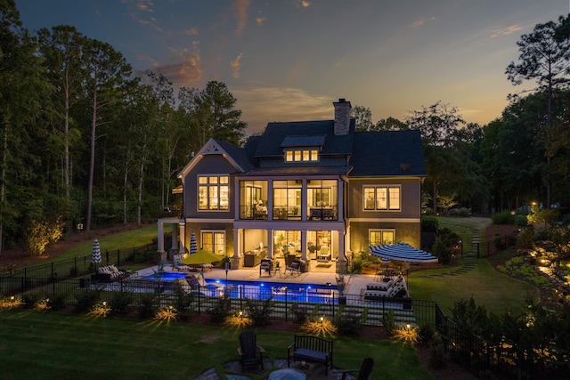 back house at dusk featuring a patio, a balcony, a lawn, an outdoor hangout area, and a fenced in pool