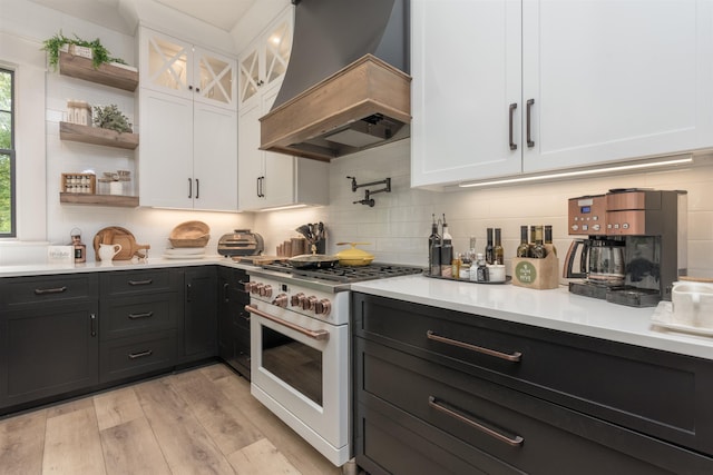 kitchen with premium range hood, high end stove, white cabinets, decorative backsplash, and light hardwood / wood-style floors