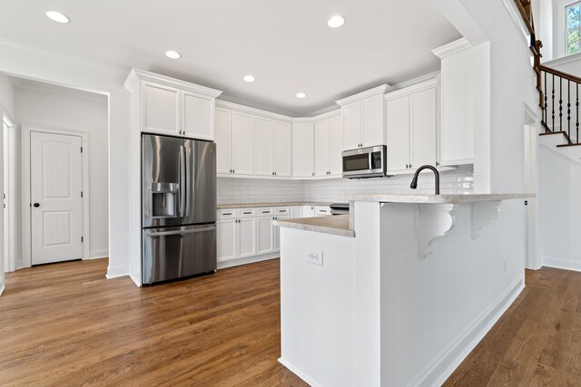 kitchen with white cabinetry, dark hardwood / wood-style flooring, a breakfast bar area, and appliances with stainless steel finishes