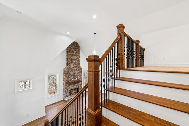 stairway featuring wood-type flooring, a fireplace, and high vaulted ceiling