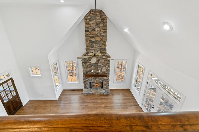 unfurnished living room with hardwood / wood-style flooring, a stone fireplace, high vaulted ceiling, and ceiling fan