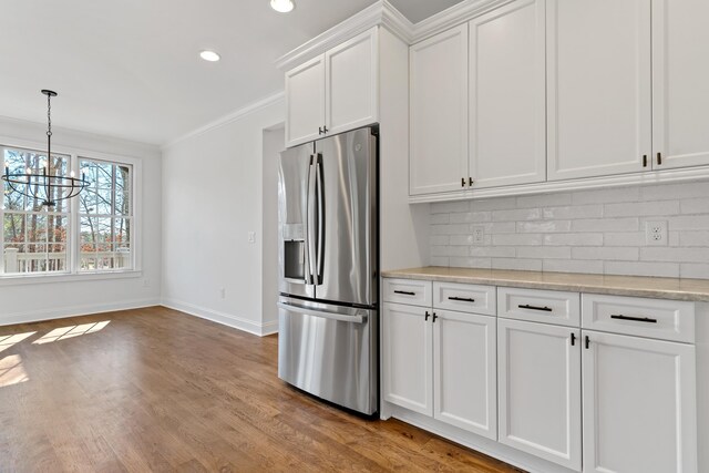 kitchen featuring ornamental molding, stainless steel fridge, white cabinets, light stone countertops, and backsplash