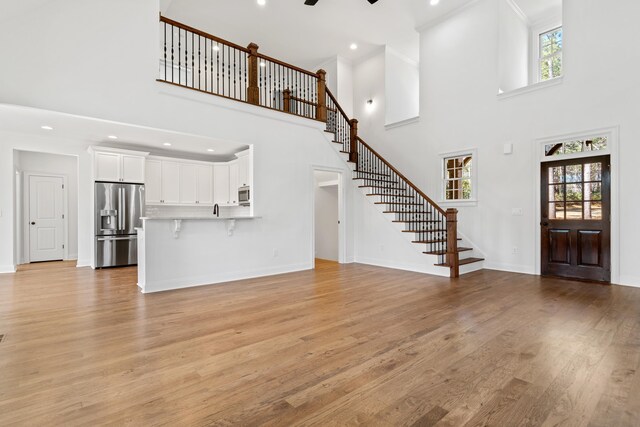 unfurnished living room with ceiling fan, a towering ceiling, and light hardwood / wood-style floors