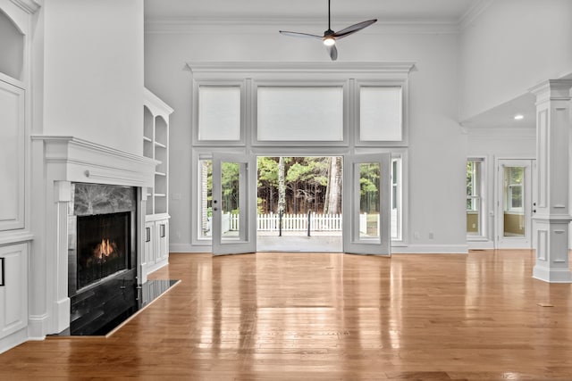 unfurnished living room featuring ornate columns, a high ceiling, a high end fireplace, and light wood-type flooring