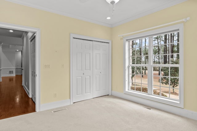 unfurnished bedroom featuring light carpet, crown molding, multiple windows, and a closet