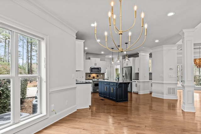 kitchen with blue cabinetry, hanging light fixtures, a kitchen island, stainless steel appliances, and decorative columns