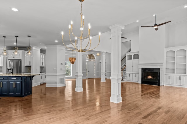 living room featuring ceiling fan, decorative columns, a high ceiling, ornamental molding, and light wood-type flooring