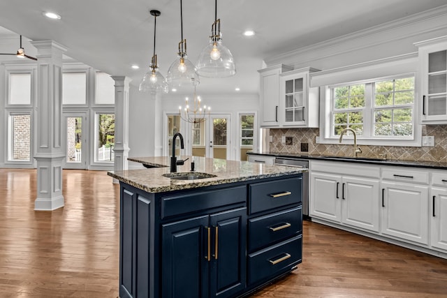 kitchen featuring sink, white cabinetry, a center island with sink, blue cabinets, and ornate columns