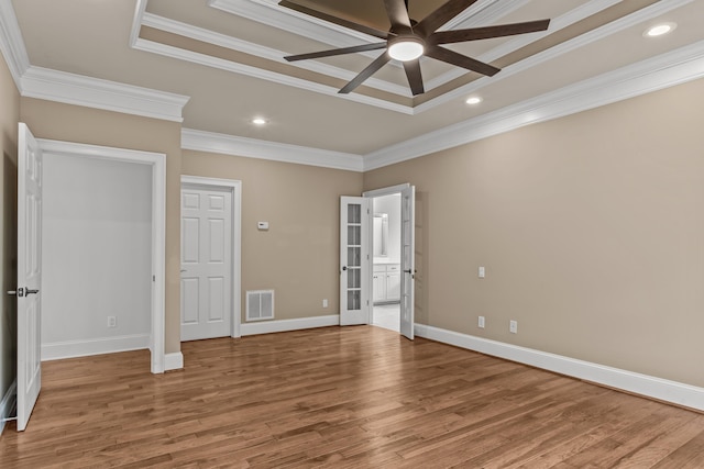 unfurnished bedroom with wood-type flooring, ceiling fan, a tray ceiling, crown molding, and ensuite bath