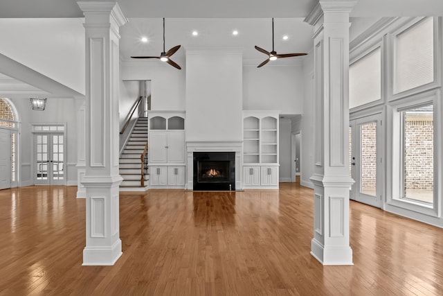 unfurnished living room with decorative columns, a high ceiling, ceiling fan, and light wood-type flooring