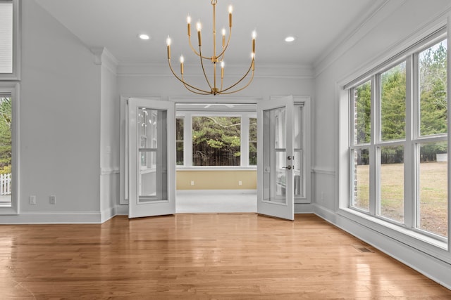 unfurnished dining area featuring ornamental molding, a notable chandelier, and light wood-type flooring