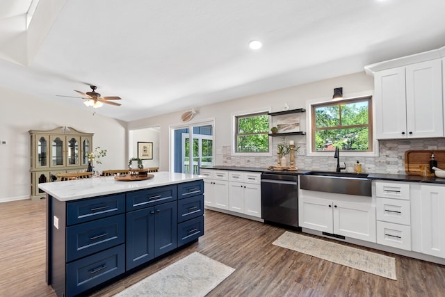 kitchen with wood finished floors, a sink, decorative backsplash, dishwasher, and blue cabinetry