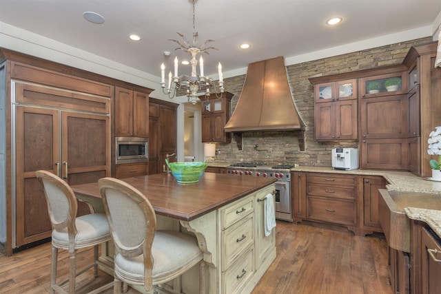 kitchen featuring premium range hood, built in appliances, a center island, dark stone countertops, and pendant lighting