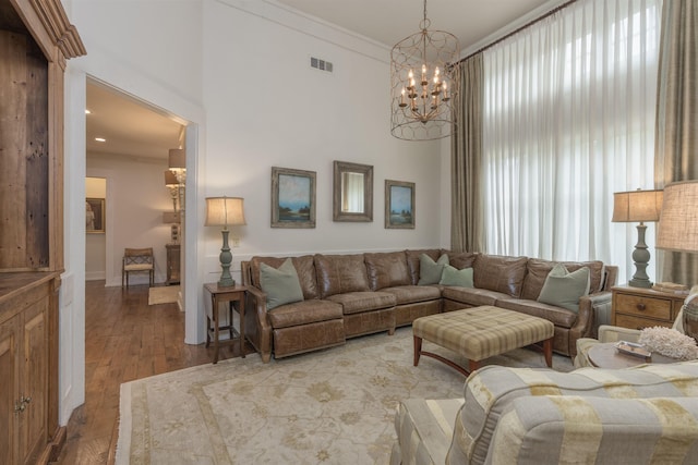 living room with crown molding, a towering ceiling, wood-type flooring, and an inviting chandelier