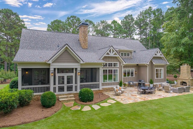 rear view of property with a lawn, a sunroom, a patio, and an outdoor living space with a fireplace