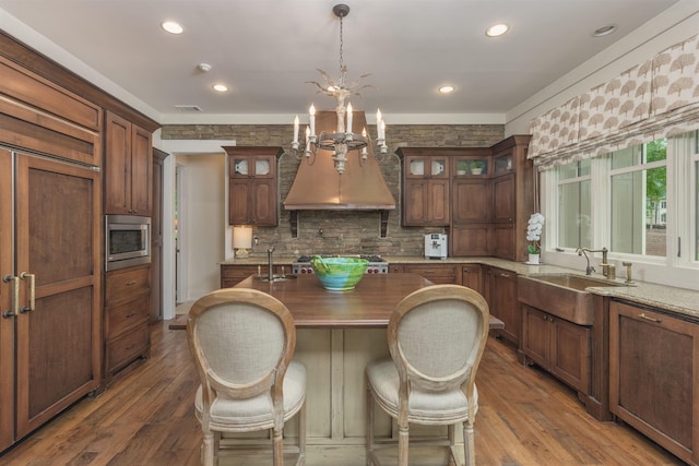 kitchen with dark wood-type flooring, premium range hood, sink, pendant lighting, and stainless steel appliances