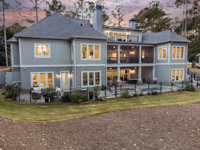 1101 Brookside, Greensboro, GA 30642 - back of house at dusk featuring a chimney, fence, a balcony, a shingled roof, and a patio