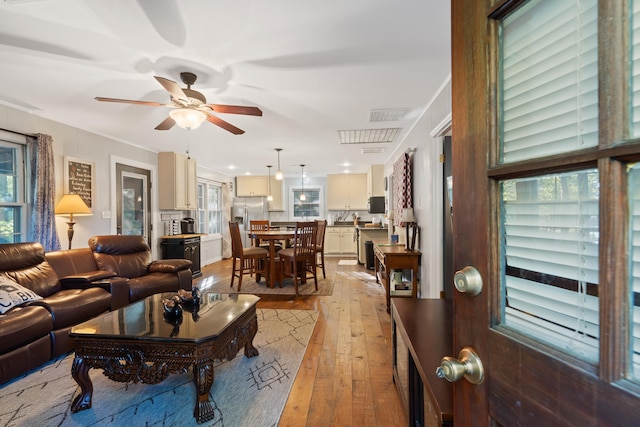 living area featuring visible vents, a healthy amount of sunlight, light wood-type flooring, and a ceiling fan