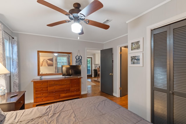 bedroom with visible vents, wood finished floors, a closet, crown molding, and ceiling fan