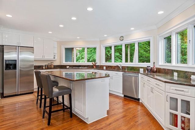 kitchen with sink, dark stone countertops, stainless steel appliances, white cabinets, and a kitchen island