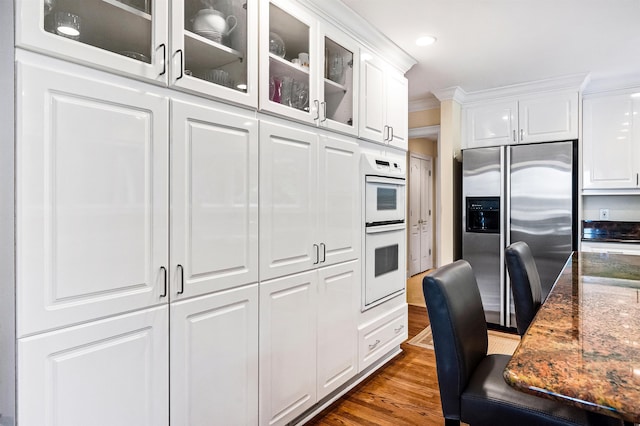 kitchen featuring white cabinetry, stainless steel fridge with ice dispenser, dark hardwood / wood-style floors, double oven, and dark stone counters