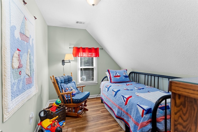 bedroom with vaulted ceiling, hardwood / wood-style floors, and a textured ceiling