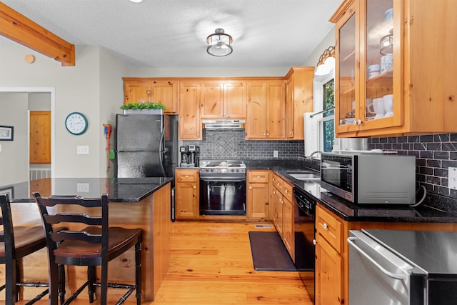 kitchen featuring sink, a kitchen breakfast bar, black appliances, dark stone counters, and light wood-type flooring