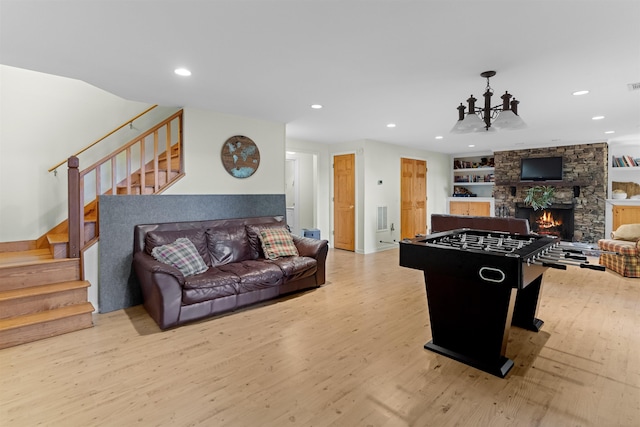 playroom featuring built in shelves, an inviting chandelier, a fireplace, and light hardwood / wood-style flooring