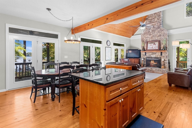 kitchen featuring a breakfast bar area, a center island, a wealth of natural light, a stone fireplace, and dark stone counters