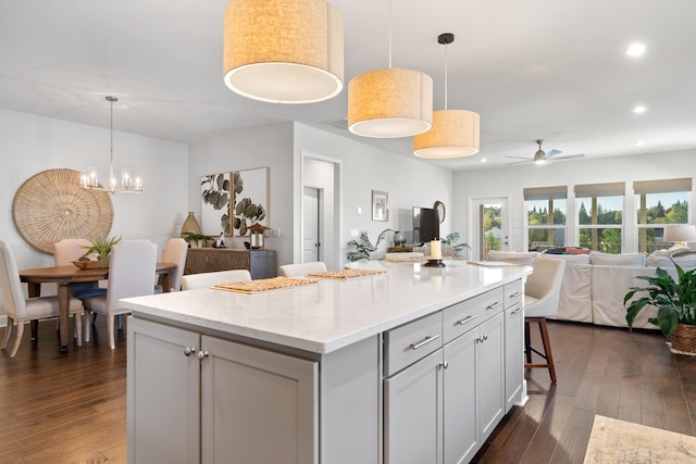 kitchen featuring ceiling fan with notable chandelier, pendant lighting, dark hardwood / wood-style flooring, a kitchen breakfast bar, and a center island