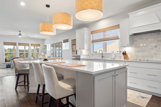 kitchen with decorative light fixtures, sink, white cabinets, a kitchen breakfast bar, and a center island