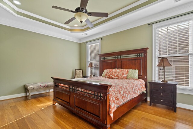 bedroom featuring ornamental molding, a tray ceiling, and light wood-type flooring