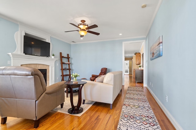 living room with crown molding, ceiling fan, a tile fireplace, and light hardwood / wood-style flooring