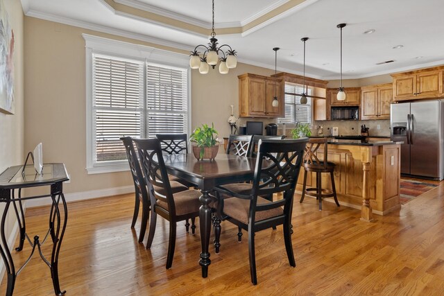 dining space featuring a raised ceiling, ornamental molding, and light hardwood / wood-style flooring