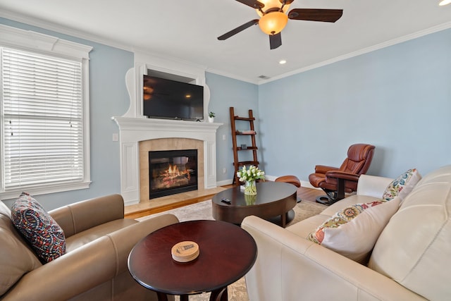 living room featuring a tile fireplace, crown molding, ceiling fan, and light hardwood / wood-style flooring