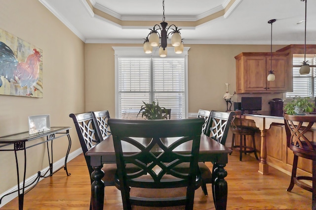 dining room with crown molding, a tray ceiling, and light wood-type flooring