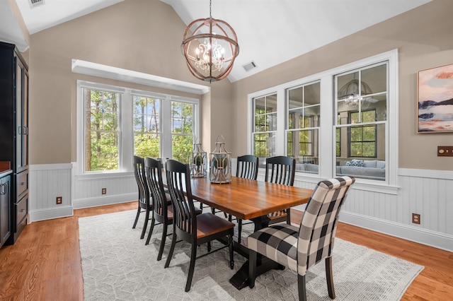 dining room featuring a healthy amount of sunlight, a chandelier, vaulted ceiling, and light wood-type flooring